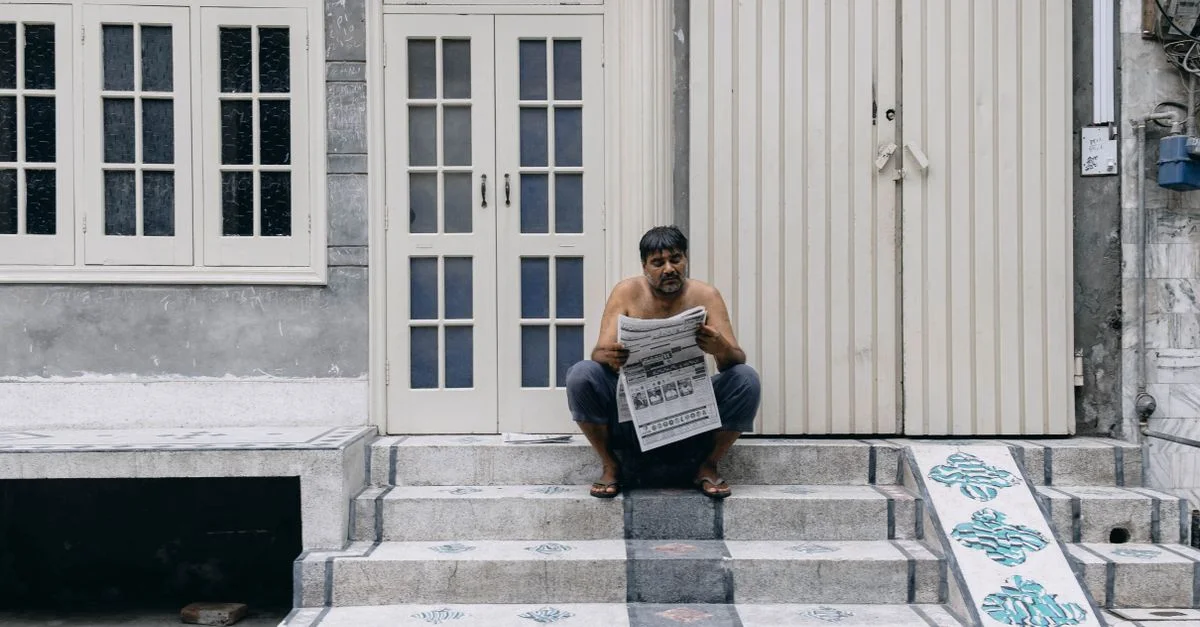 Un homme assis sur des escaliers lisant un journal devant un bâtiment à Faisalabad, Punjab, Pakistan.