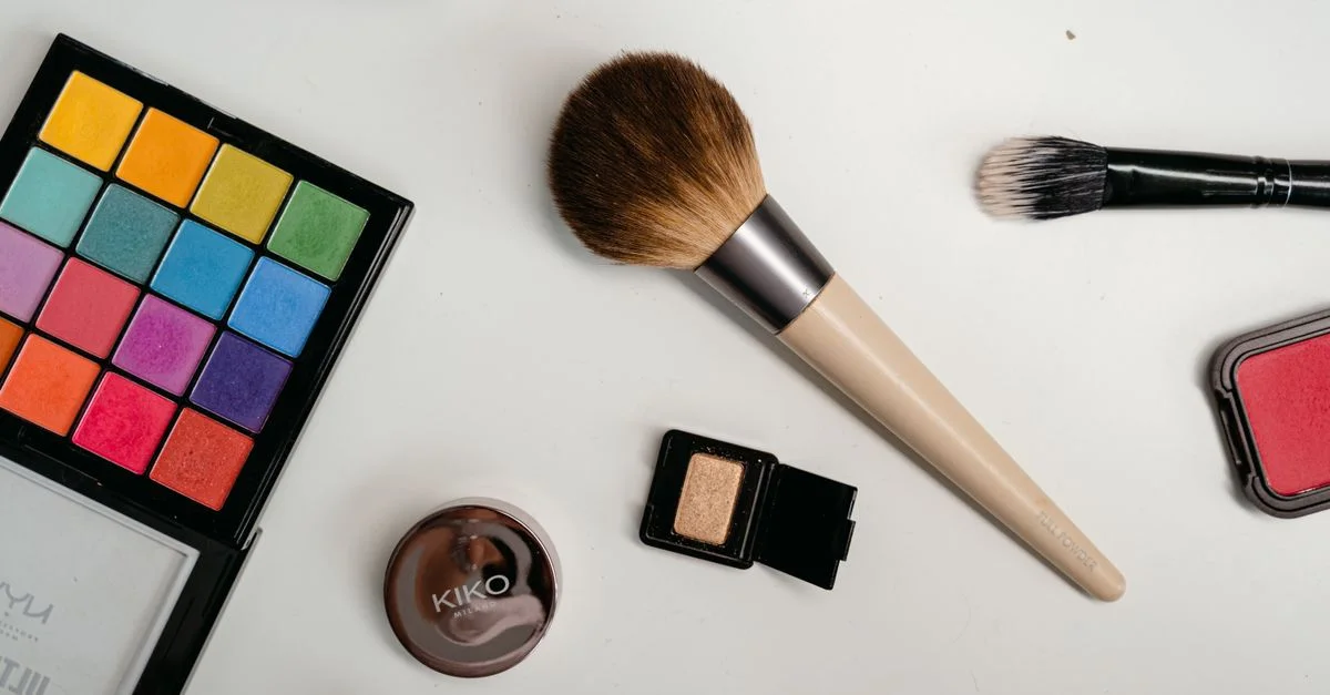 Un arrangement dynamique d'essentiels de maquillage comprenant une palette colorée et des pinceaux sur une surface blanche.