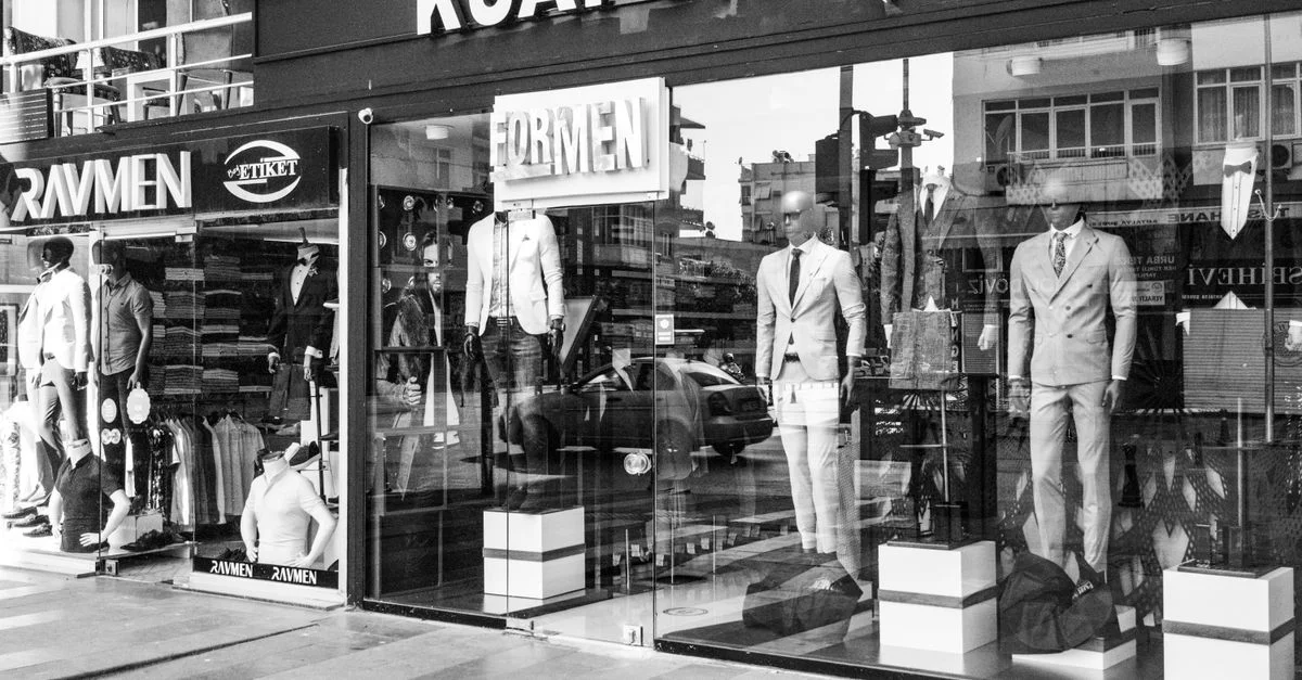 Image en noir et blanc d'une vitrine de mode masculine présentant des costumes élégants avec des mannequins en évidence.